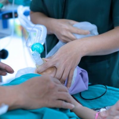 A small child is held by medical staff with a mask with tubes over their nose and mouth